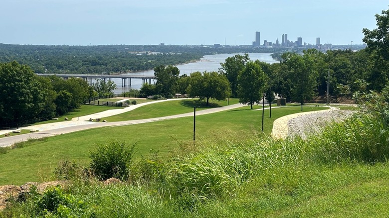 Colinas cubiertas de hierba con árboles y senderos para caminar en Chandler Park con vista al agua y al horizonte de la ciudad de Tulsa en Oklahoma