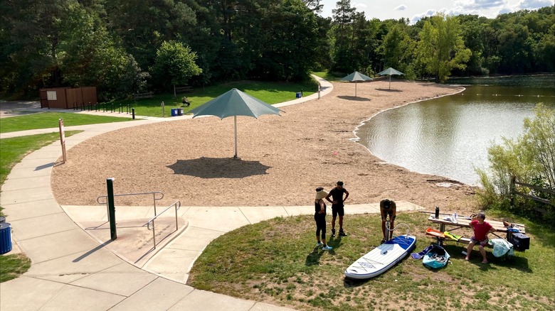 Playa de arena en el lago Schulze con gente preparándose para hacer kayak en el Parque Regional Lebanon Hills, Minnesota