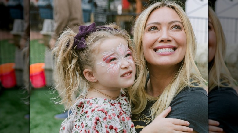 Hilary Duff lleva su cabello rubio liso mientras sonríe y sostiene a su hija Banks en su fiesta de tercer cumpleaños.