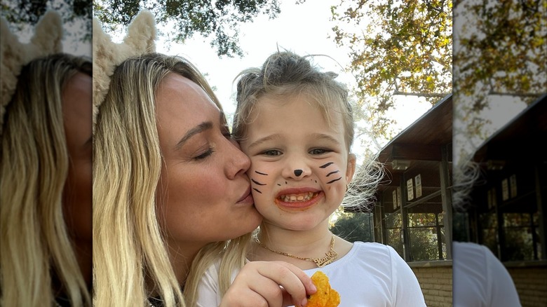 Hilary Duff usa orejas de gato con su cabello rubio suelto mientras besa a su hija Banks en la mejilla celebrando Halloween.