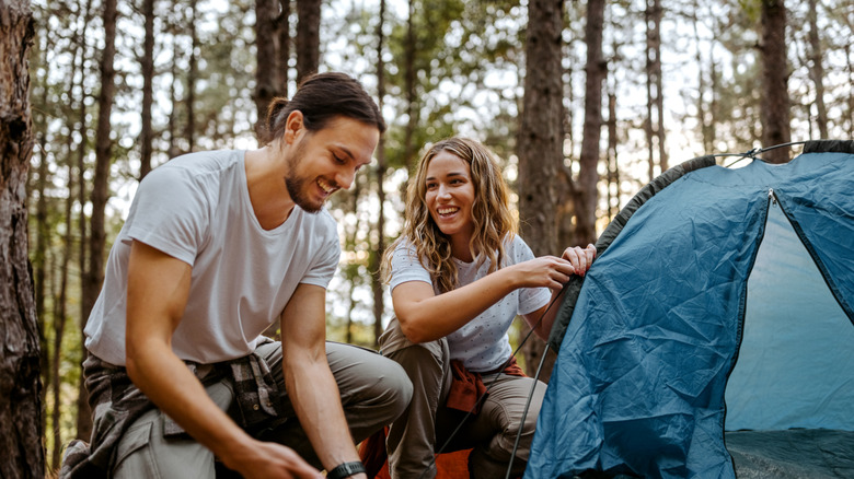 Dos campistas felices montan una tienda de campaña en el bosque.