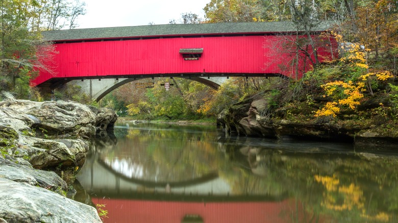 Puente cubierto de madera roja Narrows reflejado en Sugar Creek en Turkey Run State Park