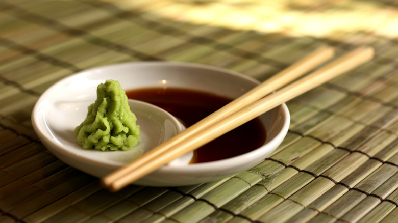 Un plato de salsa de soja y wasabi con palillos para mojar sushi en una estera de bambú enrollada