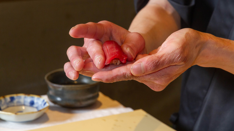 Las manos de un chef de sushi dando forma cuidadosamente a un pequeño trozo de nigiri
