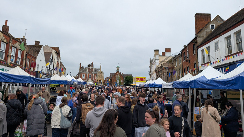 El bullicioso mercado Leighton Buzzard estaba repleto de gente, puestos de tiendas de campaña a ambos lados de la calle y edificios históricos de ladrillo detrás de ellos y al final de la calle.
