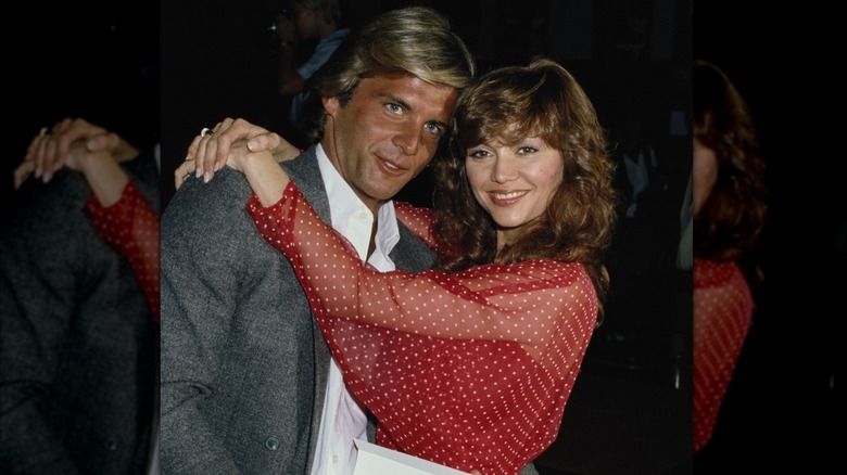 Victoria Principal con un top transparente de lunares rojos y blancos abrazando a Christopher Skinner alrededor de 1979.
