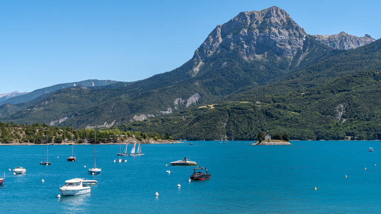 Barcos en el agua en el lago de Serre-Ponçon frente a los verdes y elevados Alpes franceses