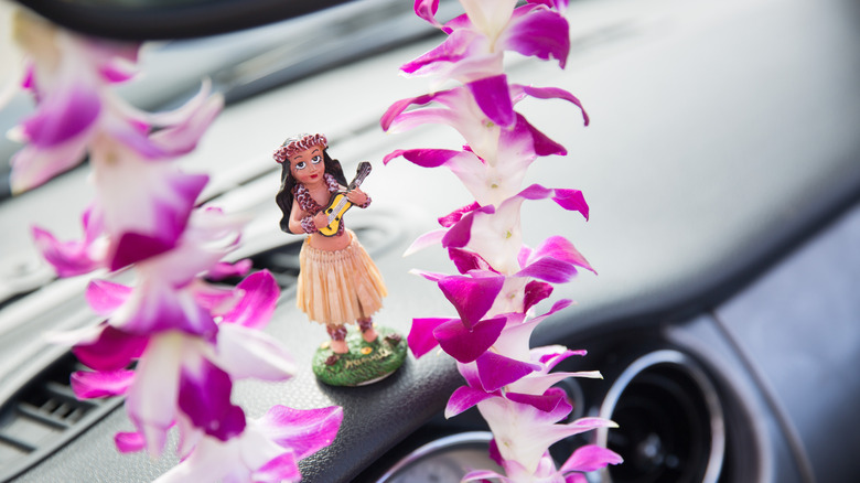 Un adorno de tablero de bailarina de hula hawaiana enmarcado por un collar de orquídeas