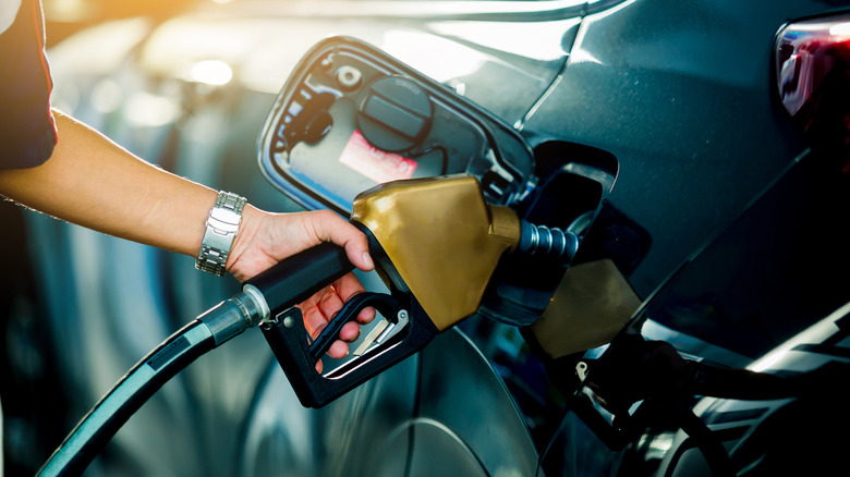 Primer plano de un brazo que sostiene una bomba de gasolina, llenando el tanque de un automóvil