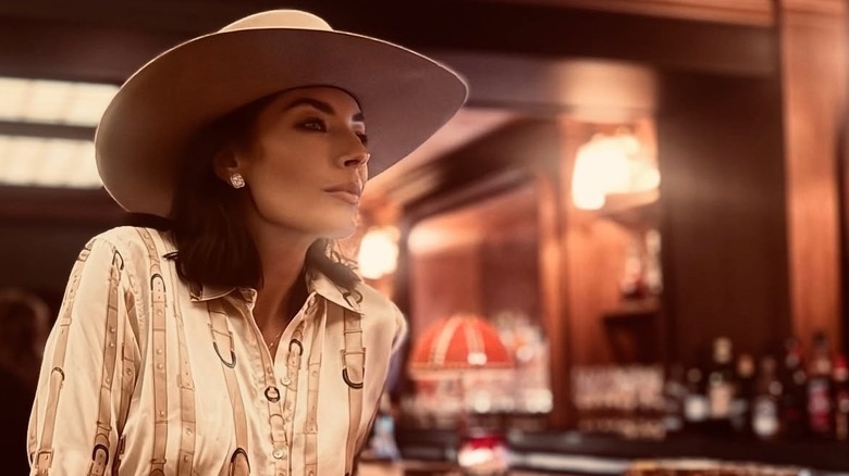 Nicole Sheridan sentada en un bar con una camisa de estilo occidental y un sombrero de vaquero.