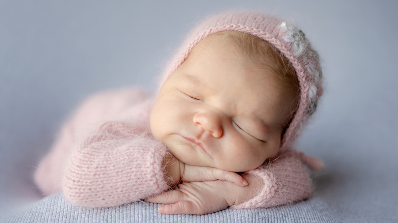 Un bebé recién nacido durmiendo con un traje rosa y un gorro.
