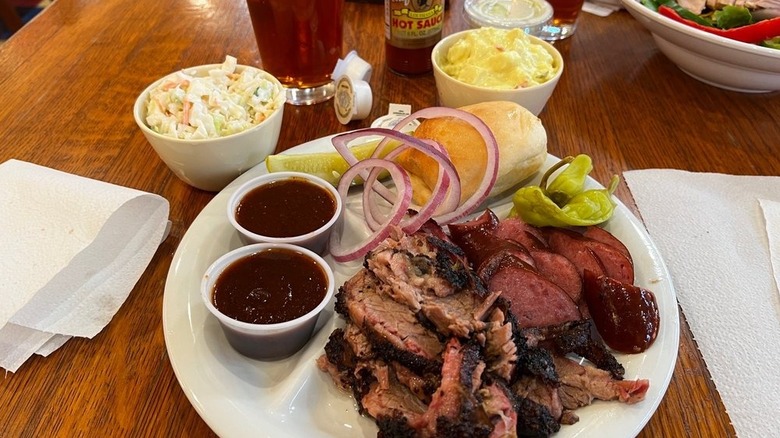 Un plato de selecciones de carne a la barbacoa y salsa con panecillo y guarniciones de ensalada de col y ensalada de patatas
