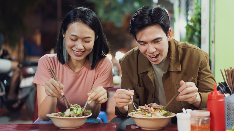 Pareja cavando en tazones de pho con cucharas y palillos