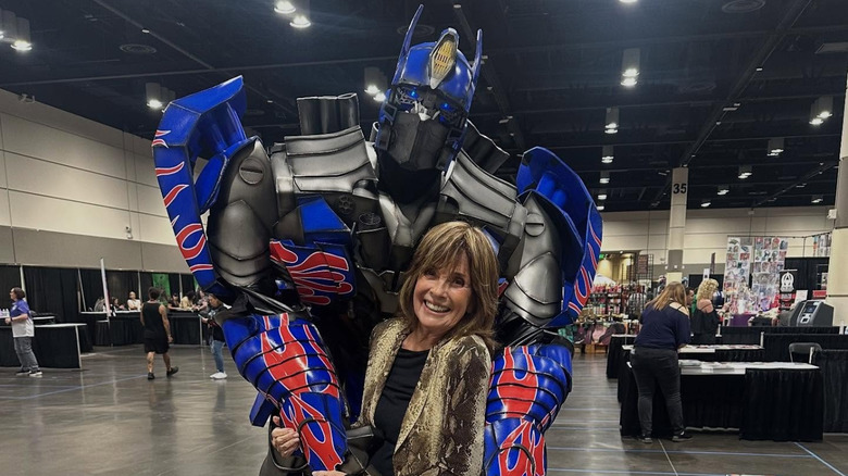 Linda Gray posa con alguien disfrazado de Transformers en un salón de eventos