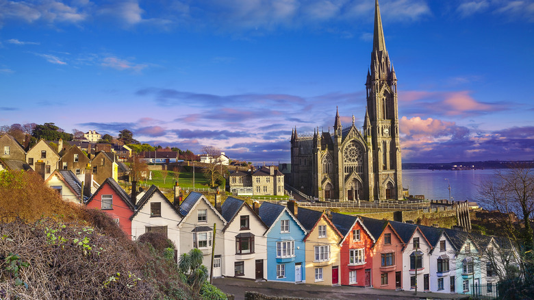 Una hilera de casas de colores brillantes a lo largo de una calle empinada frente a una catedral en Cobh.