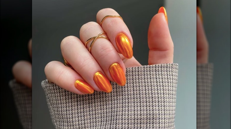 Manicura corta y redonda con esmalte de uñas cromado naranja.