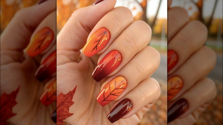 Manicura cuadrada naranja con diseños de hojas otoñales.