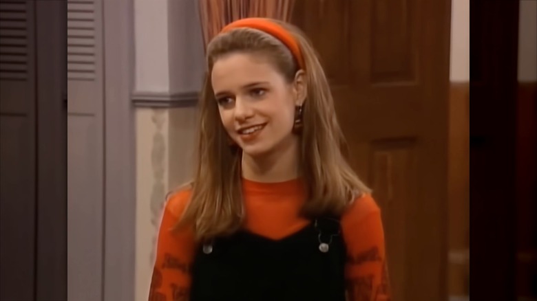 Andrea Barber con diadema naranja, top naranja y peto negro