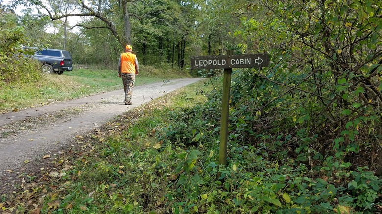 Hombre vestido con equipo de caza sendero con cartel a la cabaña Leopold en Missouri