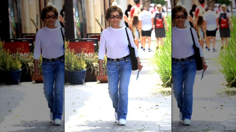 Judy Sheindlin con jeans acampanados y una manga larga blanca con un cinturón negro