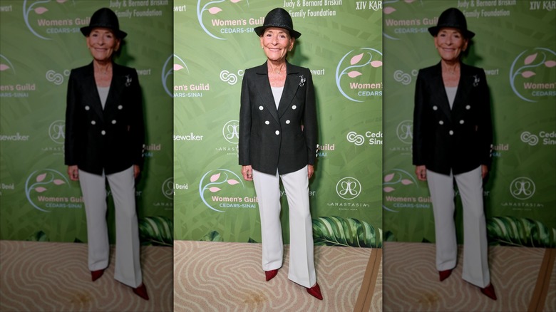 Judy Sheindlin con un sombrero fedora negro y un traje pantalón negro y crema.