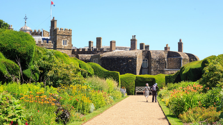 Dos personas paseando por un sendero flanqueado por parterres de flores en los terrenos del Castillo de Walmer en Walmer, Kent