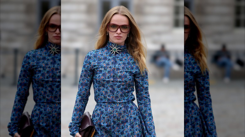 Una chica rubia con un vestido azul floral y un broche adornado.