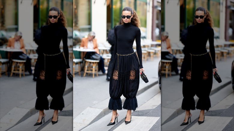Una chica morena que llevaba un cinturón de cadena dorada con pantalones negros y un jersey de cuello alto negro.