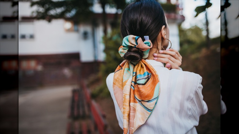 Una mujer morena con el pelo recogido en un moño y un coletero estilo bandana.