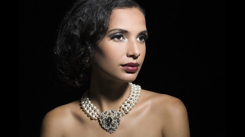 Una mujer morena con un bob y una gargantilla de perlas y cristales.