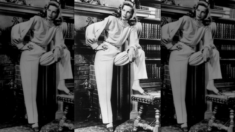 Lauren Bacall posa cerca de una chimenea con un suéter de cuello alto de Leah Rhodes, pantalones holgados y mules de cuña en diciembre de 1946.