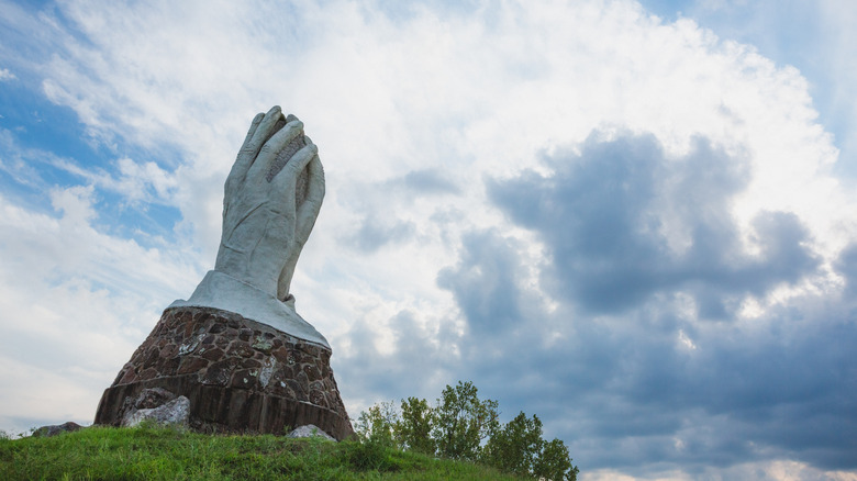 Una estatua de estuco que representa manos orando en King Jack Park en Webb City, frente a un cielo nublado