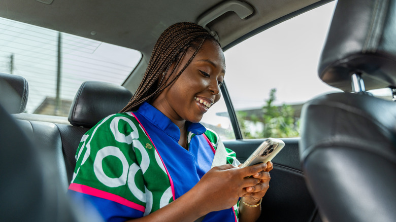 una mujer sonriente sentada en el asiento trasero con su teléfono