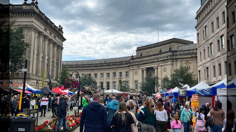 La gente pasaba por puestos de comida flanqueados por edificios de piedra con columnas en Bolton.