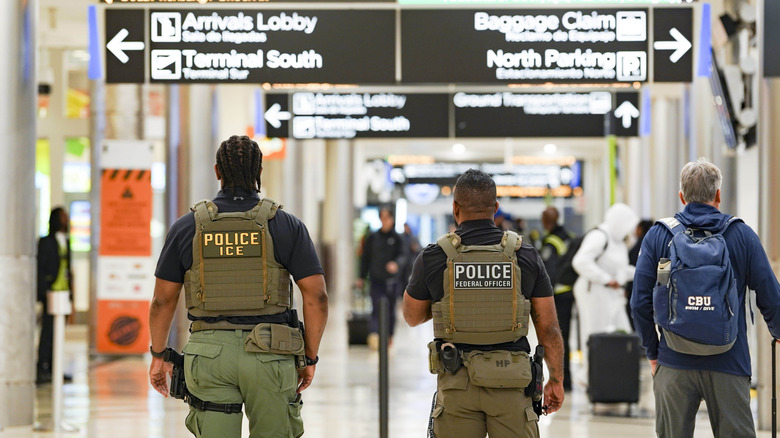 Agentes de ICE desde atrás caminan por el aeropuerto