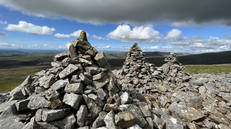 Tres montones de piedra dispuestas en conos redondos, con verdes colinas en la montaña Gragareth, Inglaterra