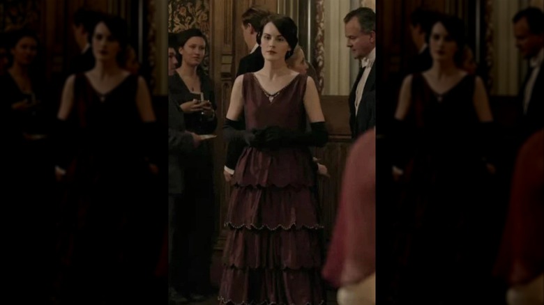 Michelle Dockery como Lady Mary con un vestido sin tirantes color burdeos y guantes largos negros