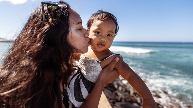 Una mamá besando a su bebé frente al mar