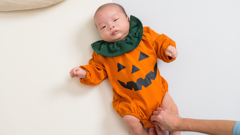 Un bebé con un mameluco de calabaza.