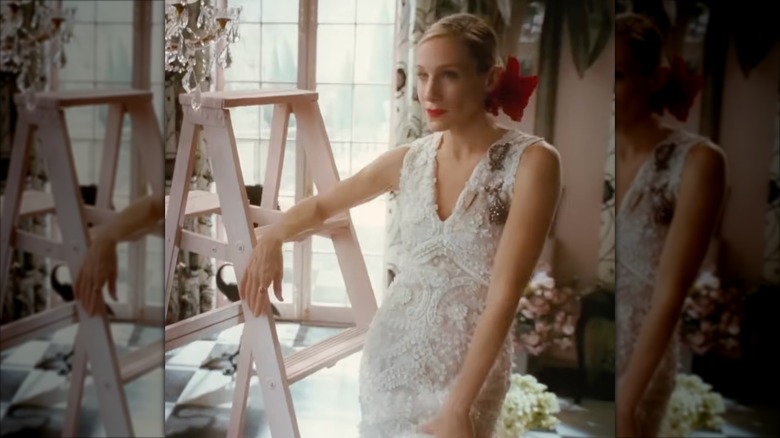 Sarah Jessica Parker como Carrie Bradshaw con un vestido de novia de encaje con cola de pez y una flor roja en el pelo.