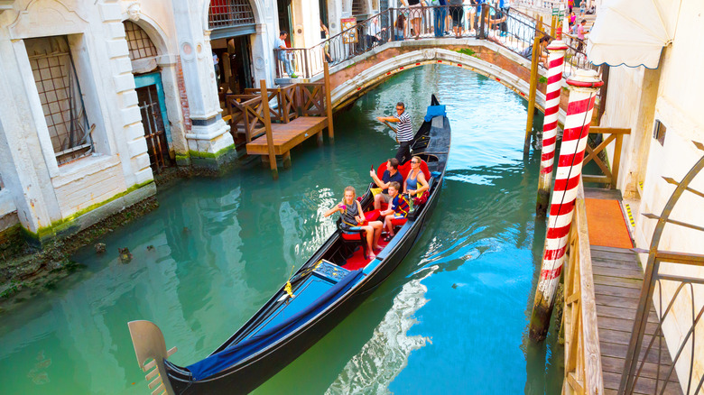 Un grupo de personas en una góndola pasa por debajo del puente en un canal estrecho en Venecia