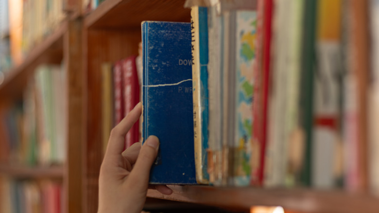 Un desenfocado muestra una estantería con una mano sacando uno de los libros.