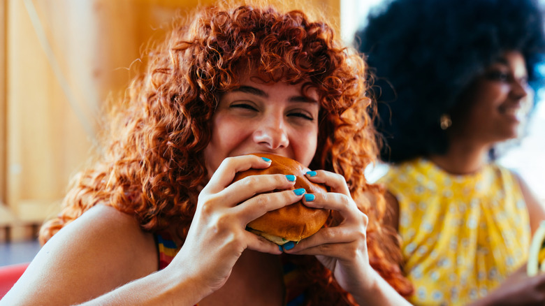 Una mujer feliz muerde una hamburguesa
