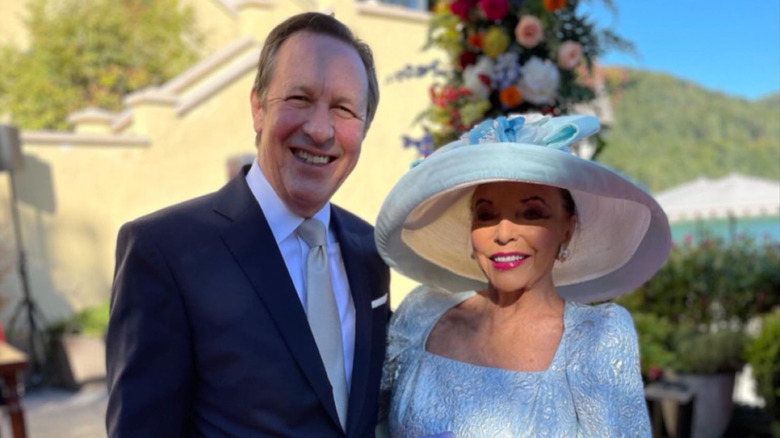 Joan Collins con vestido azul y sombrero con Percy Gibson